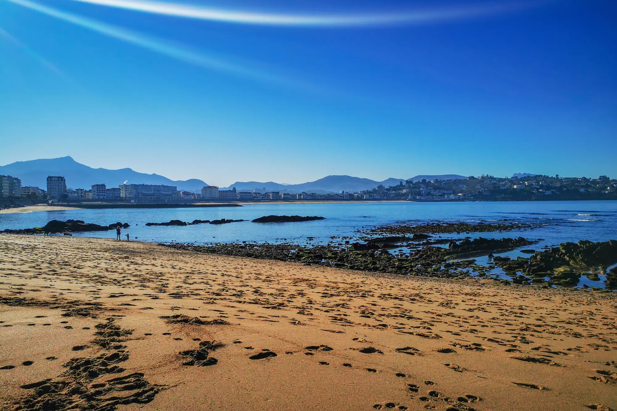 Plage de sable avec vue sur montagne et océan.