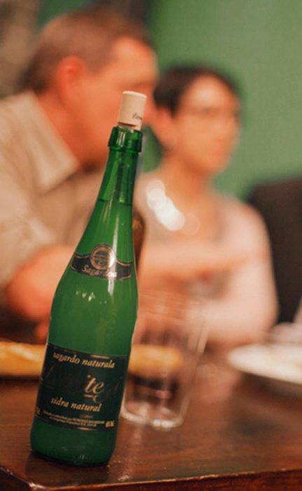 Bouteille de cidre vert sur table avec personnes floues.